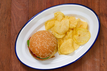 hamburger with potato chips on white dish on brown background