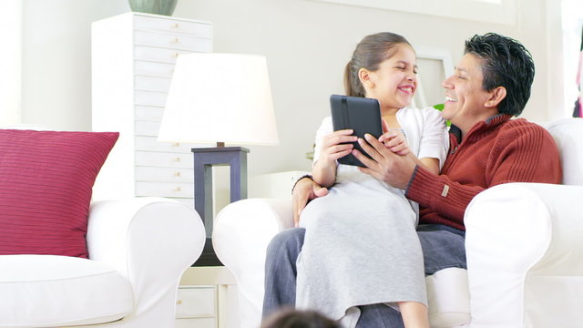 A cute daughter sits on her Dad's lap as they go over a digital tablet together