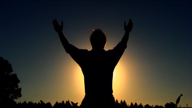 Man Kneeling and Raising his Hands at Sunset