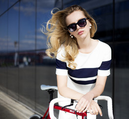 Fototapeta na wymiar blonde costs in city in sun glasses with bicycle