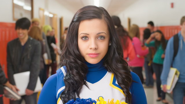 A female student dressed as a cheerleader stands in a hallway with other kids