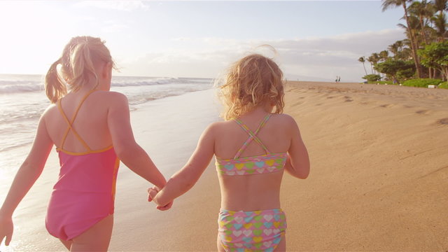 Two sisters walk down the beach together swinging their arms back and forth