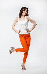 Happy playful young woman in orange pants posing on neutral back