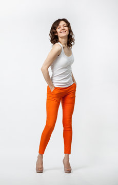 Happy smiling young woman in orange pants posing on neutral back