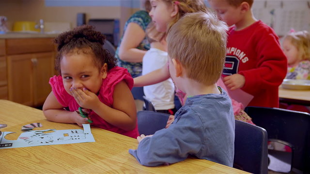 Two cute school children work on a project at a table together during art class