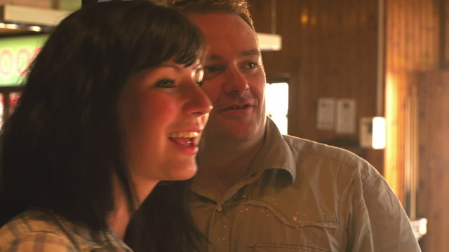 Close up of a couple throwing darts then hugging at a bar