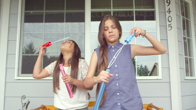 Two sisters sitting on a bench on their porch stand up and start making bubbles