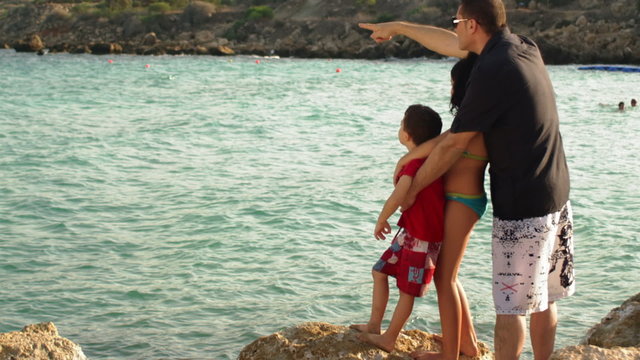 A father pointing out in the ocean to his kids