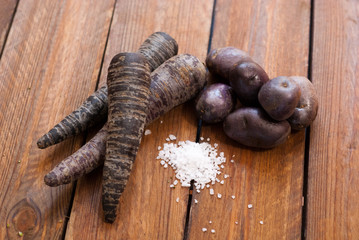 purple carrots and purple potatoes with salt on raw wooden table
