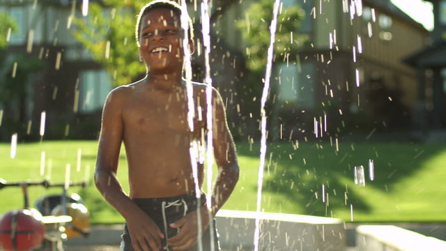 A young boys play in a water fountain at a park during the summer