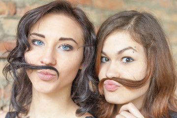 Two young pretty girls making mustache of their hair