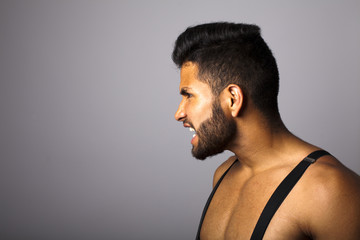 Joven latino con barba y tirantes de perfil gritando