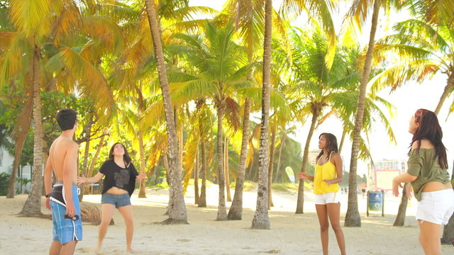 A group of four teenagers play ball in a circle at the beach