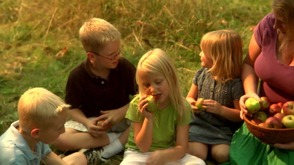 A group of young children sit on the grass and eat apples