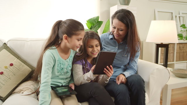 A mother and her two daughters sit and play with tablets and and smile