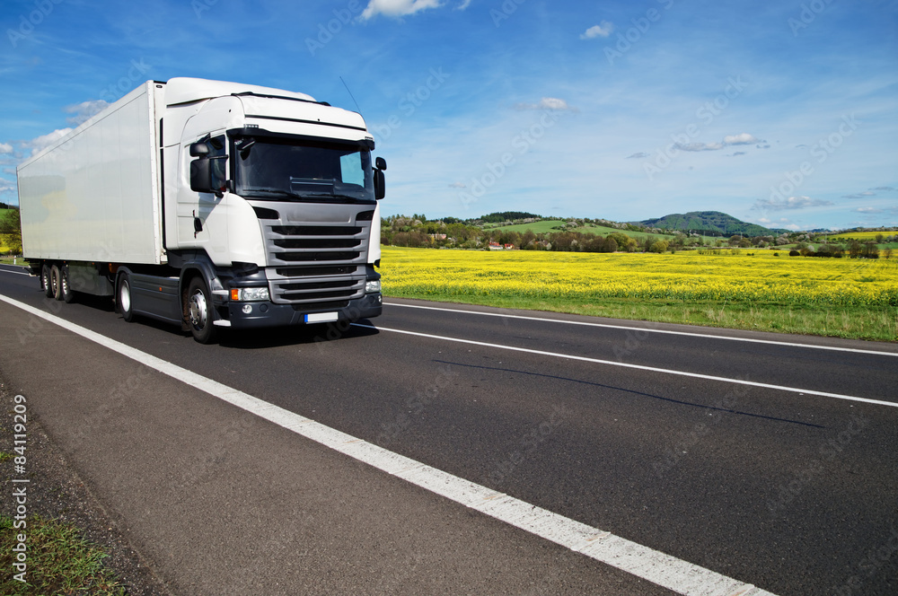 Wall mural white truck on the road between yellow flowering rapeseed field