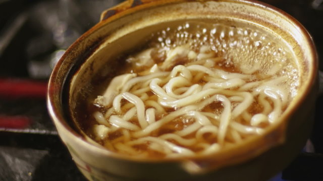 Medium shot of noodles being cooked is small bowl over flame