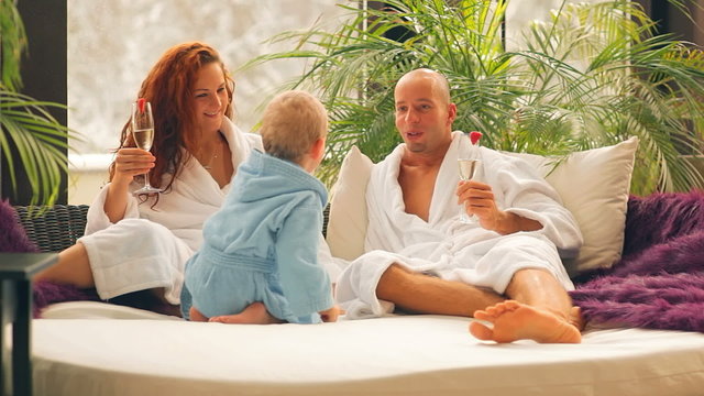 A young couple relax in white robes with their son and have Champaign
