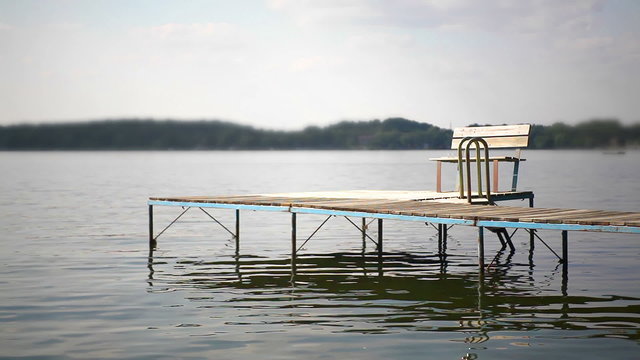 Shot of a wooden dock and bench extending out into the water on a lake