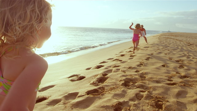 Young girls on a beach run to there mom and give her a big hug as the sun sets 