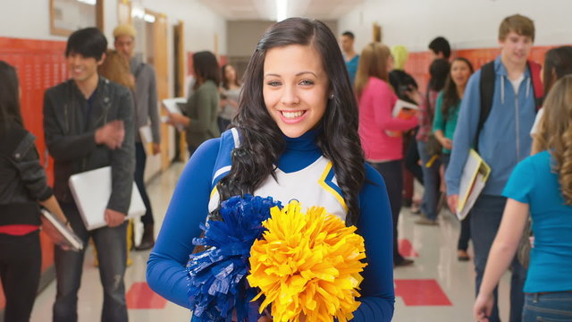 A female student dressed as a cheerleader stands in a hallway with other kids