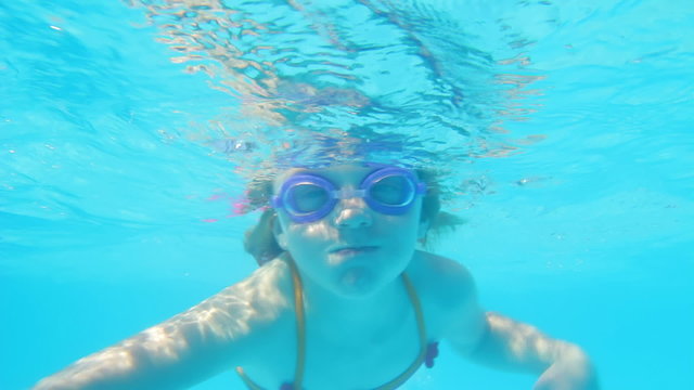 A young girl dives underwater and looks into the camera