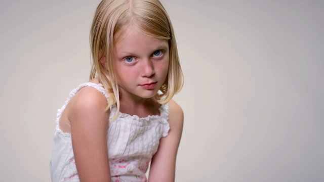 Young blonde girl pulls a sad face against a white background