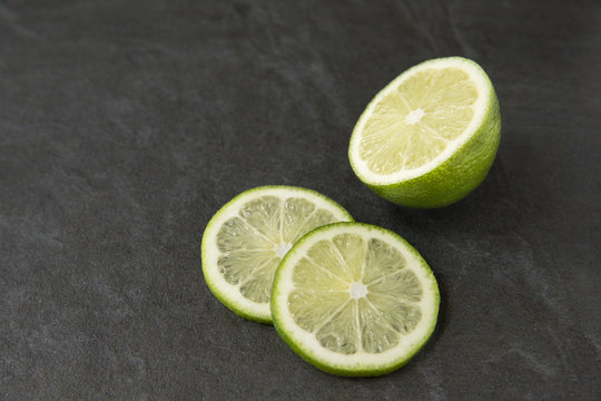 Half of a lime with two slices on slate background