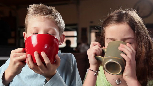 Two young kids drink cocoa and get whipped cream on their noses and laugh