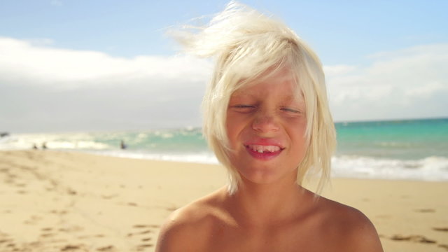 A boy blows into a conch shell while at the beach and smiles into the camera