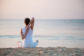 Fototapeta na wymiar Young woman doing exercises sitting on sea coast at dawn
