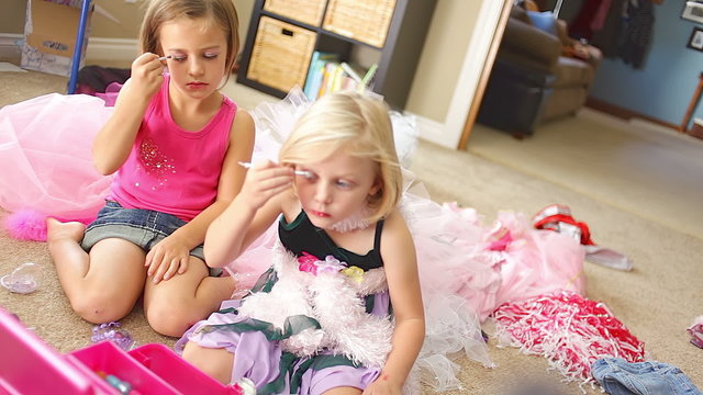 Two young girls play dress up and put make up on themselves