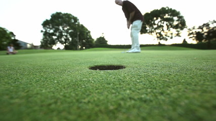 A male golfer sinks a put and gets excited. Wide shot.