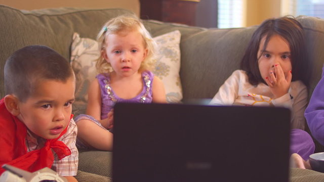 A small group of children all sit on the couch and stare intently at the TV together