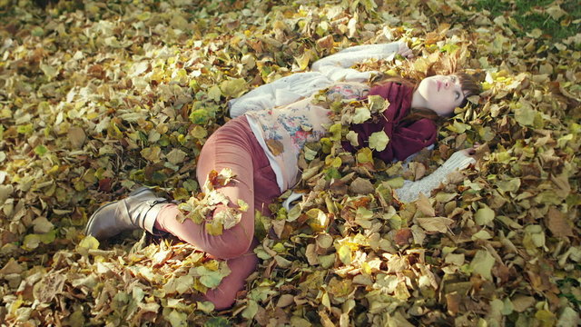 A young woman sleeping on a pile of dead leaves in the park opens her eyes and looks into the camera and smiles
