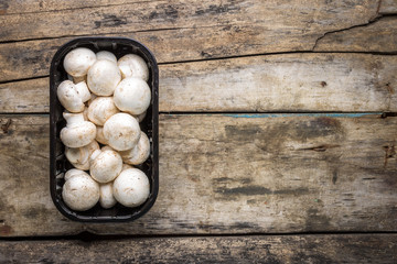 Fresh raw mushrooms in plastic container on wooden background