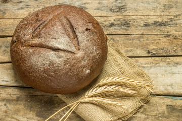 Loaf of bread with wheat grains on wooden background