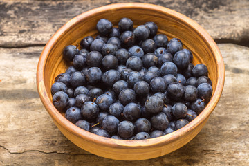 Fresh wild berries in clay bowl on wooden background.