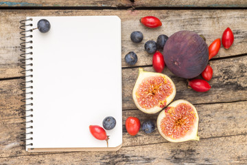 Fresh wild berries and figs with blank notebook on wood 