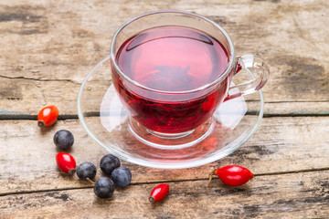 Glass Cup of red karkade tea with wild berries on wood