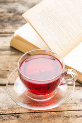 Glass Cup of hot tea with open book on old wooden table