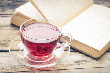 Glass cup of tea with old book on wood background