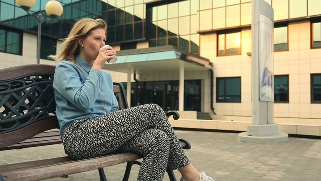 woman drinking coffee outdoors, sitting on the bench.