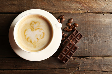 Cup of coffee latte art with grains and chocolate on wooden background