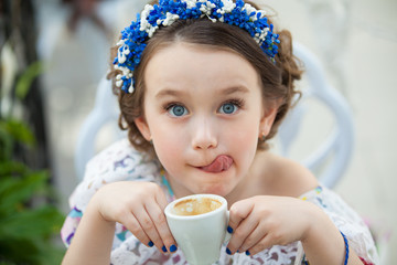 Portrait of little girl in a floral dress drinking coffee