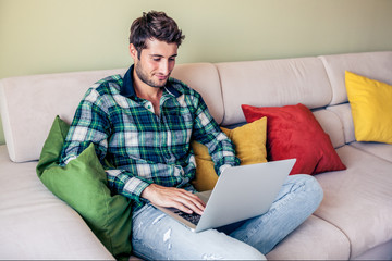Handsome young man sitting on couch working on his laptop