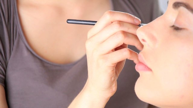 makeup artist applying eyeshadow on eyelid using makeup brush