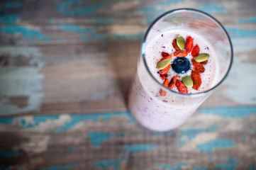 Healthy smoothie milkshake made from blended pineapple and kefir yogurt topped with pumpkin seeds, goji berries and a blueberry. Served on a rustic wooden tray, this is a healthy, nutritious breakfast - obrazy, fototapety, plakaty