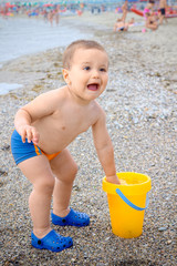 Child two year old on the beach starts crying because he dipped his hand in the water too cold bucket that filled