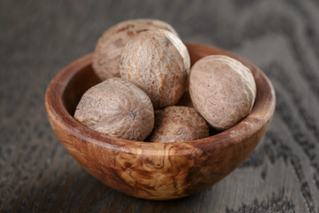 whole nutmegs in olive bowl on oak table, rustic